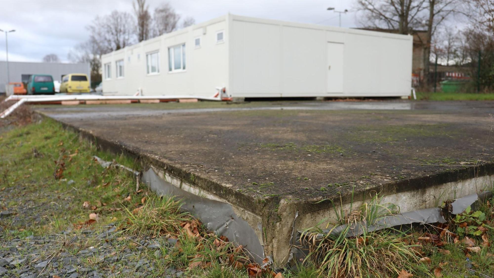 Auf einer großen Bodenplatte steht ein weißer Wohncontainer.