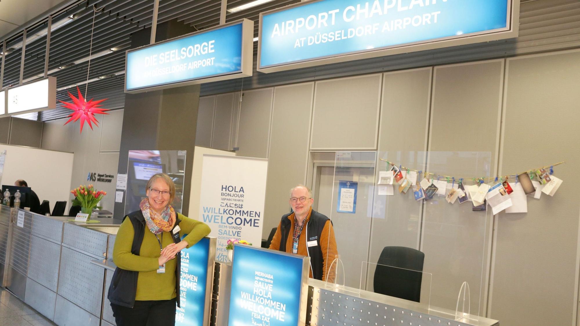 Ute Clevers und Johannes Westerdick stehen vor dem Seelsorge-Schalter am Flughafen Düsseldorf.