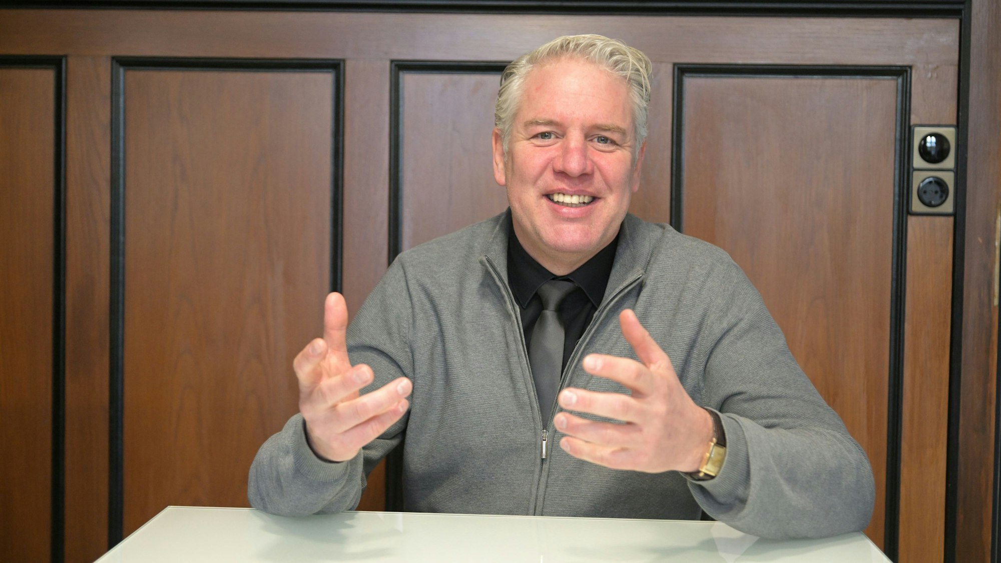 Robert Lenerts, Odenthals Bürgermeister, sitzt vor einer Holzwand an einem Tisch und gestikuliert.