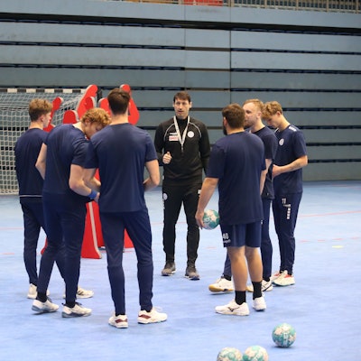 Mehrere Handballspieler des VfL Gummersbach stehen mit ihrem Co-Trainer im Kreis.