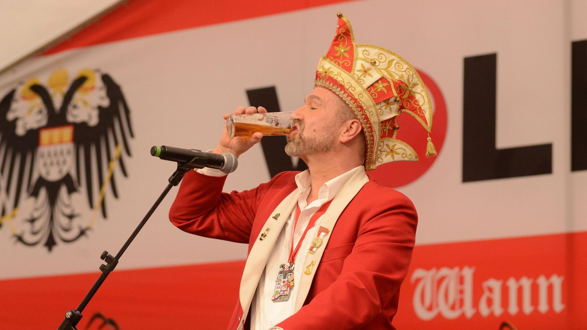 Weininger trinkt Kölsch am Rednerpult mit Mikro.
