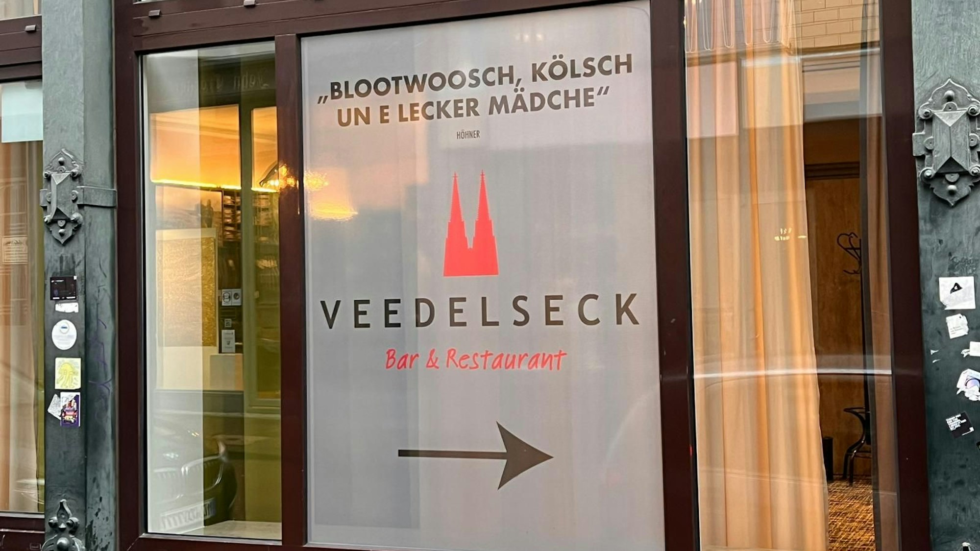 „Blotwoosch, Kölsch un e lecker Mädche“ steht auf einem Schild in einem Schaufenster.