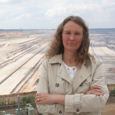 Antje Grothus steht vor dem Tagebau Hambach im Forum Terra Nova. Im Hintergrund ist ein Braunkohlebagger zu sehen. Das Foto entstand 2020.