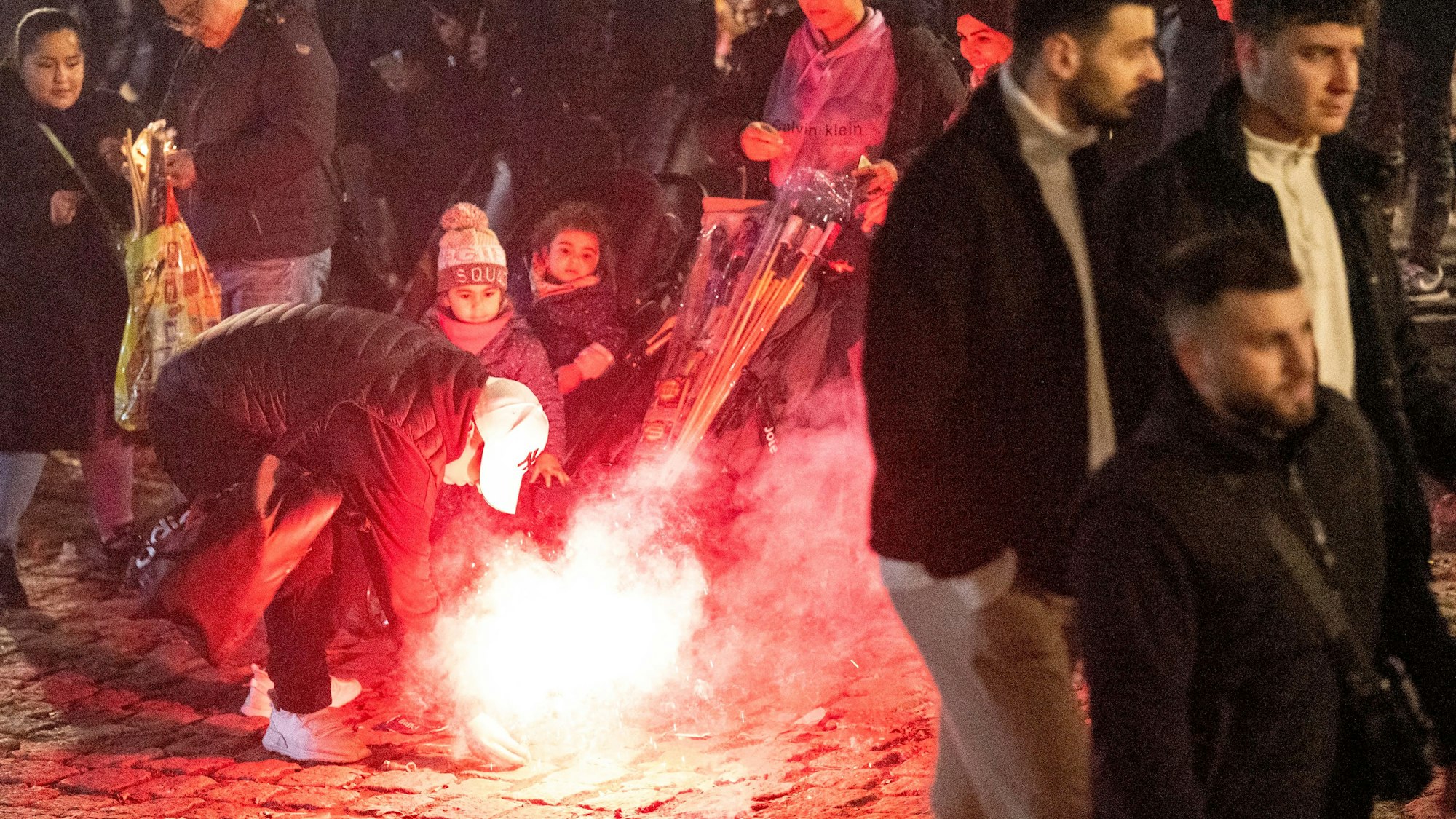 Ein Mann zündet am Silvesterabend 2022 eine Rakete mitten in einer Menschenmenge im Rheingarten in der Kölner Innenstadt