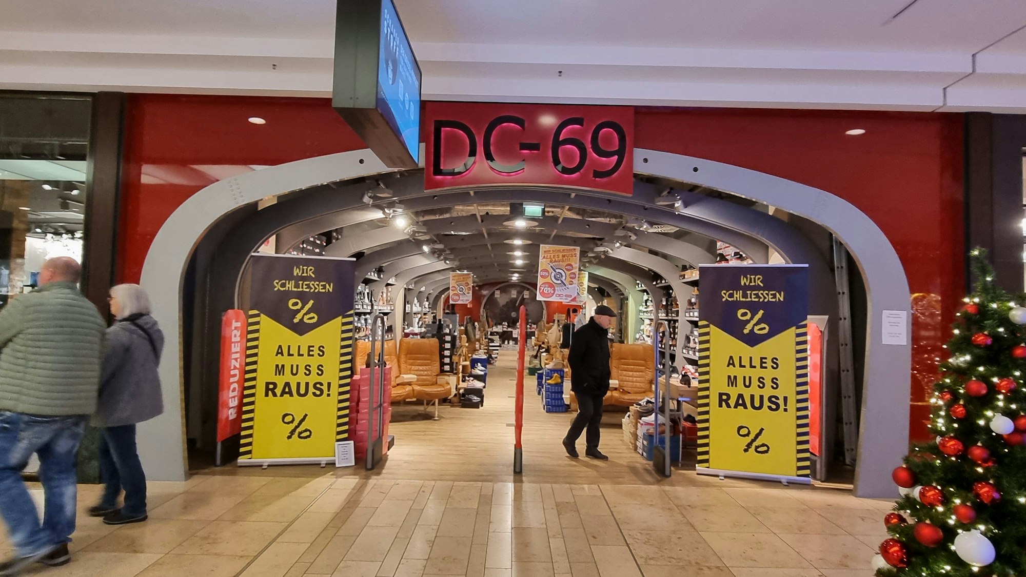 Der Eingang des Schuhgeschäfts DC-69. Links und rechts stehen Schilder mit „Wir schließen. Alles muss raus!“ Ein Mann schaut sich die Produkte an.