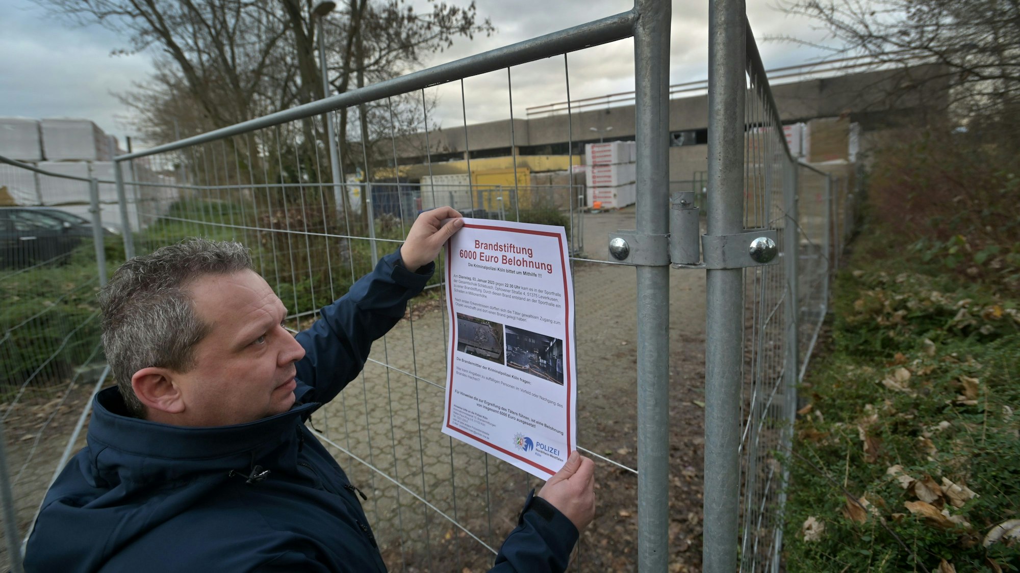 Brandermittler hängt Plakat am Bauzaun an der ausgebrannten Sporthalle der Schlebuscher Gesamtschule auf . Foto: Ralf Krieger