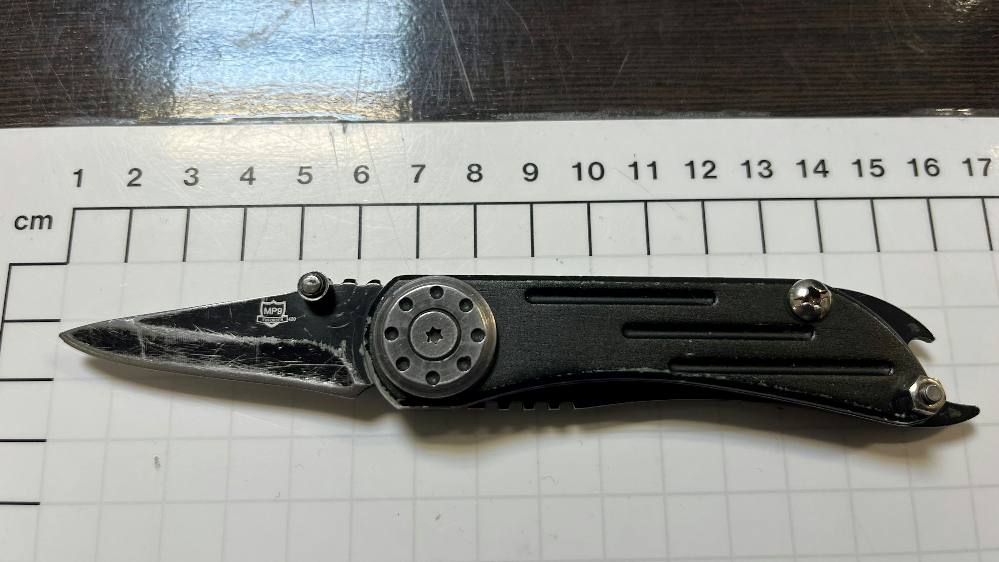 Auf einer Maßtabelle liegt ein schwarzes Messer mit aufgeklappter Klinge.