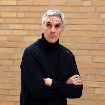 Ein Basketball-Trainer steht mit verschränkten Armen am Spielfeldrand und schaut nach oben.