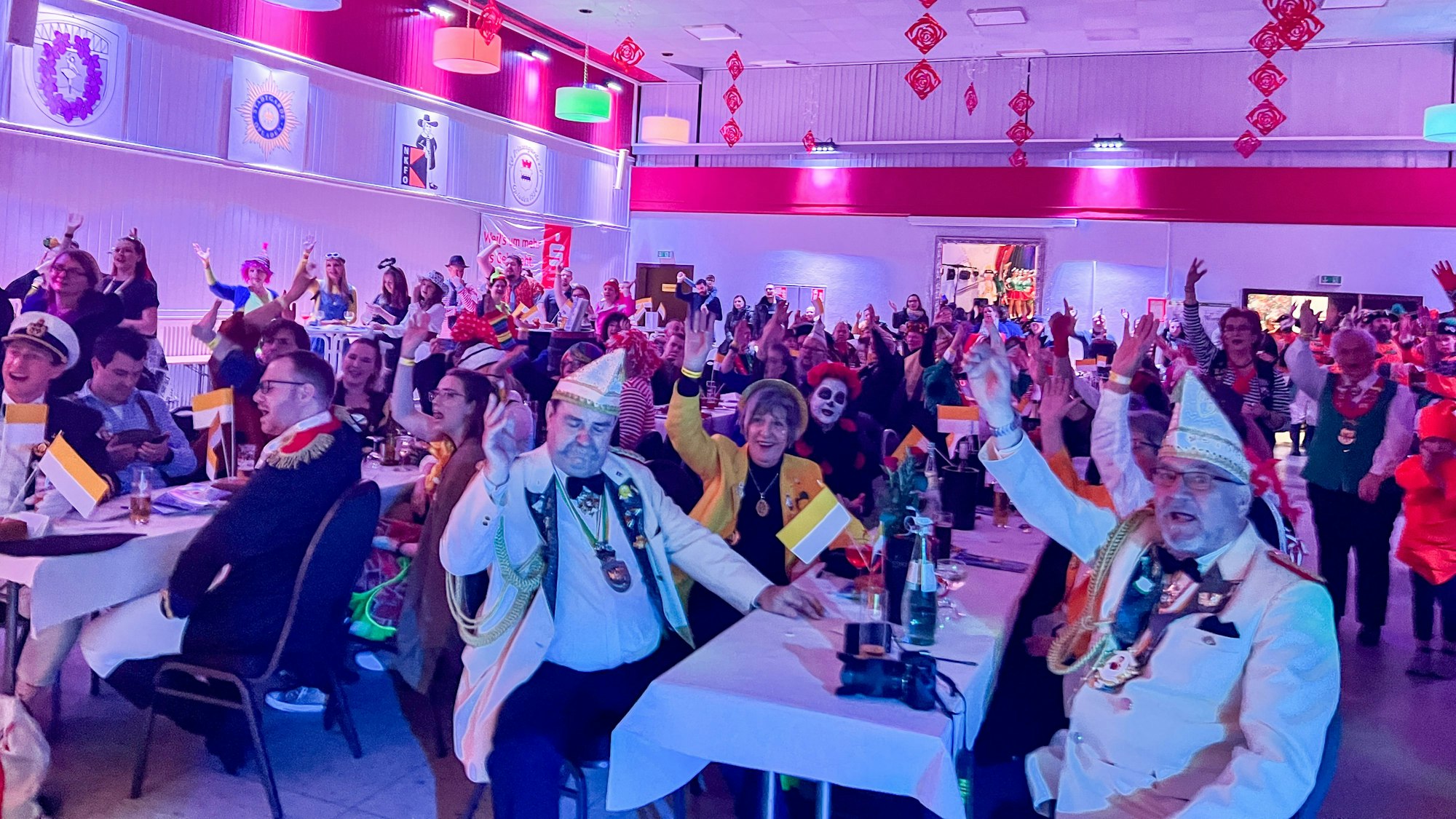 Blick in einen vollbesetzten Feiersaal, Menschen in Verkleidungen und mit Karnevalsornat feiern und applaudieren.