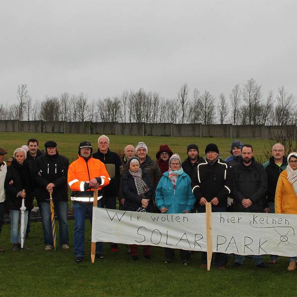 19 Anwohner haben sich mit einem Protestbanner vor der Fläche postiert, auf der ein Teil des Dahlemer Solarparks geplant ist. Auf dem Banner steht: „Wir wollen hier keinen Solarpark.“