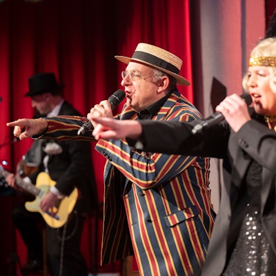 Ebasa, der Meister in gestreiftem Anzug und Mirja Boes, in Glitzerkleid und mit Haarband, moderieren die Karnevalsveranstaltung "Deine Sitzung".