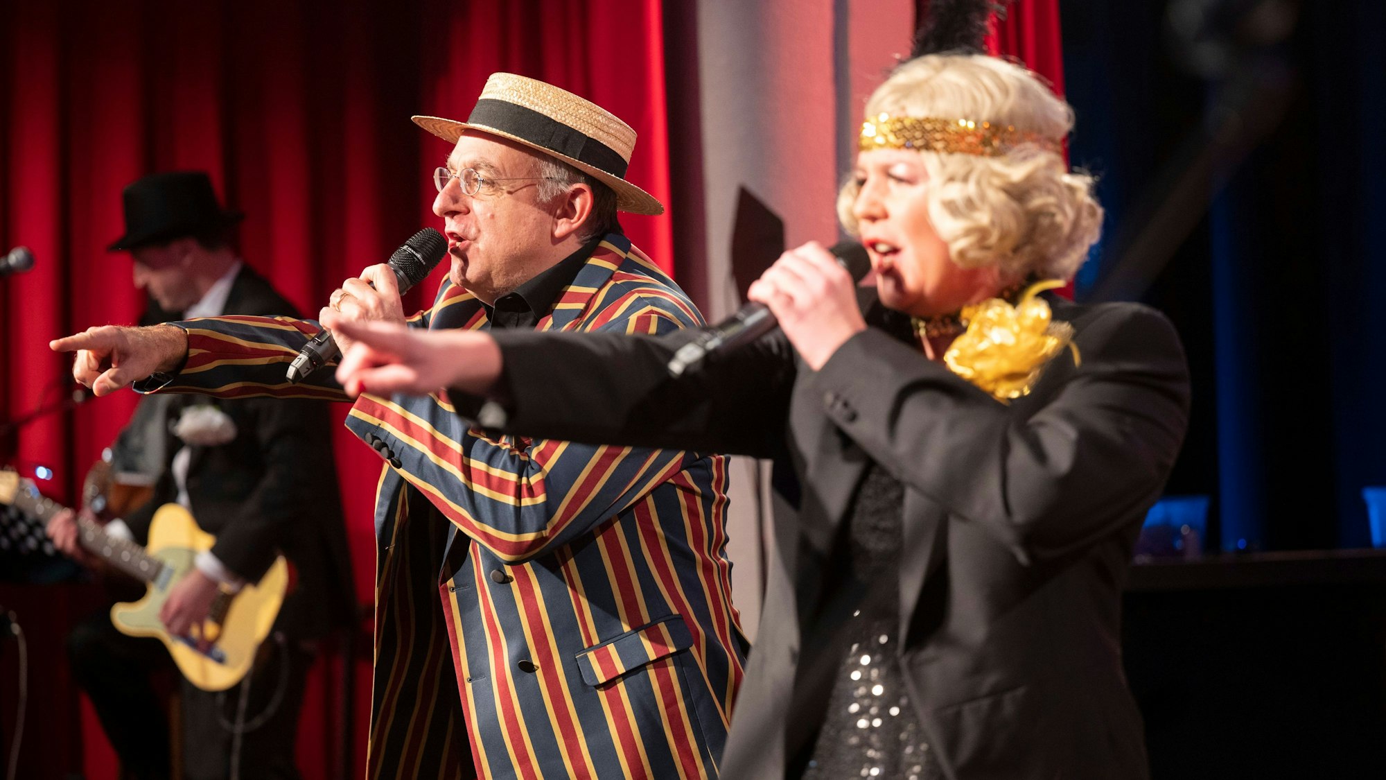 Ebasa, der Meister in gestreiftem Anzug und Mirja Boes, in Glitzerkleid und mit Haarband, moderieren die Karnevalsveranstaltung "Deine Sitzung".