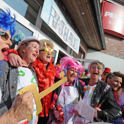 Verkleidete Frauen singen Arm in Arm mit dem 2021 verstorbenen Bürgermeister Stefan Caplan. Eine von ihnen hält einen symbolischen Stadtschlüssel in der Hand.