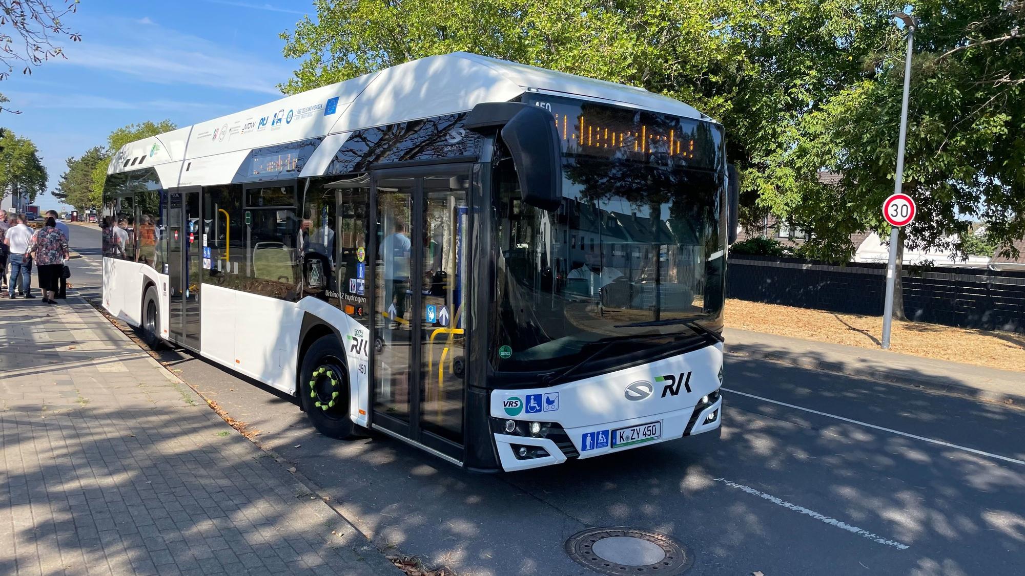 Ein weißer Omnibus der RVK steht an einer Haltestelle.