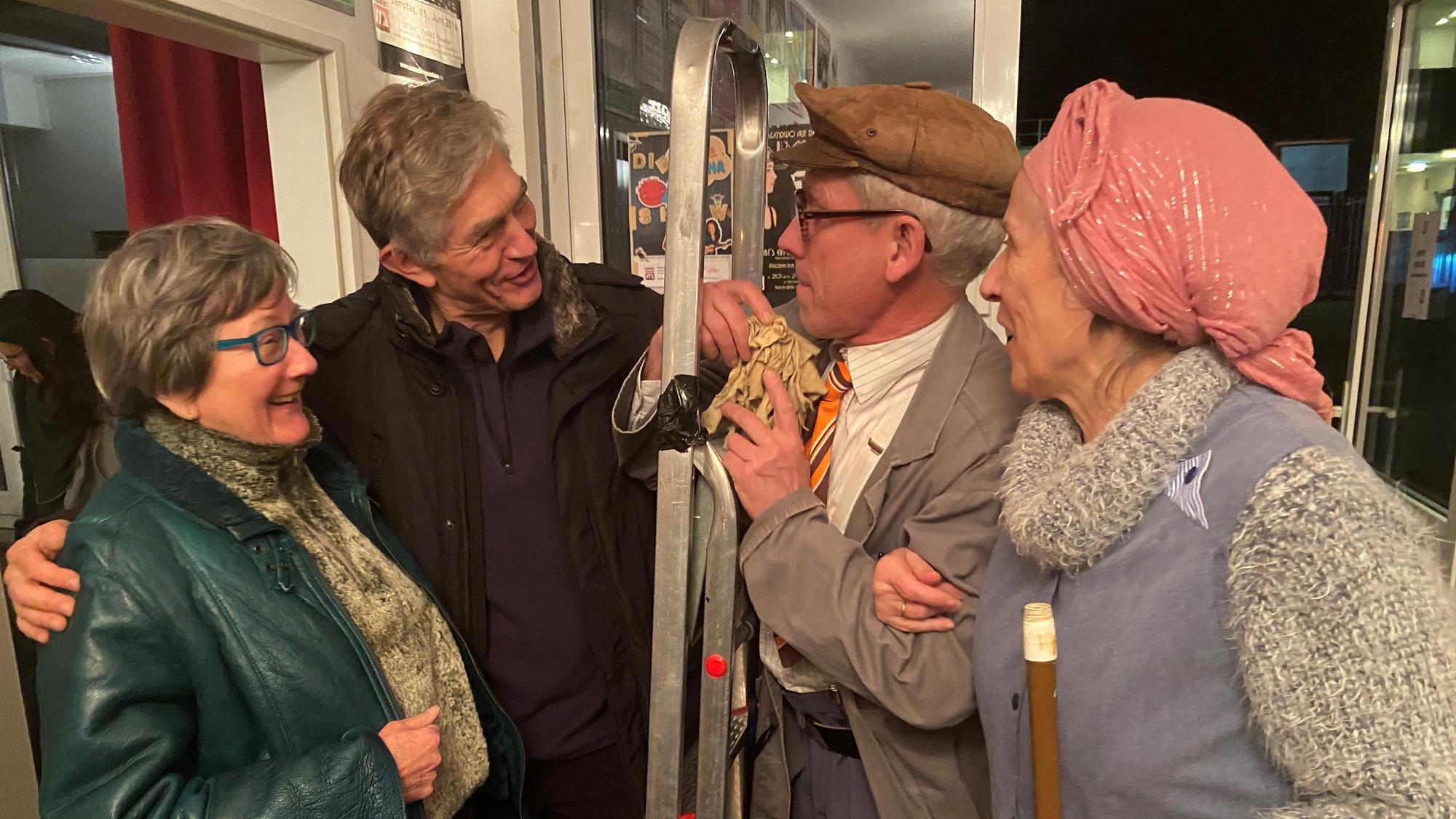 Udo Passon und Inge Weyberg stehen als Hausmeister mit Leiter und Putzfrau bei zwei Gästen.