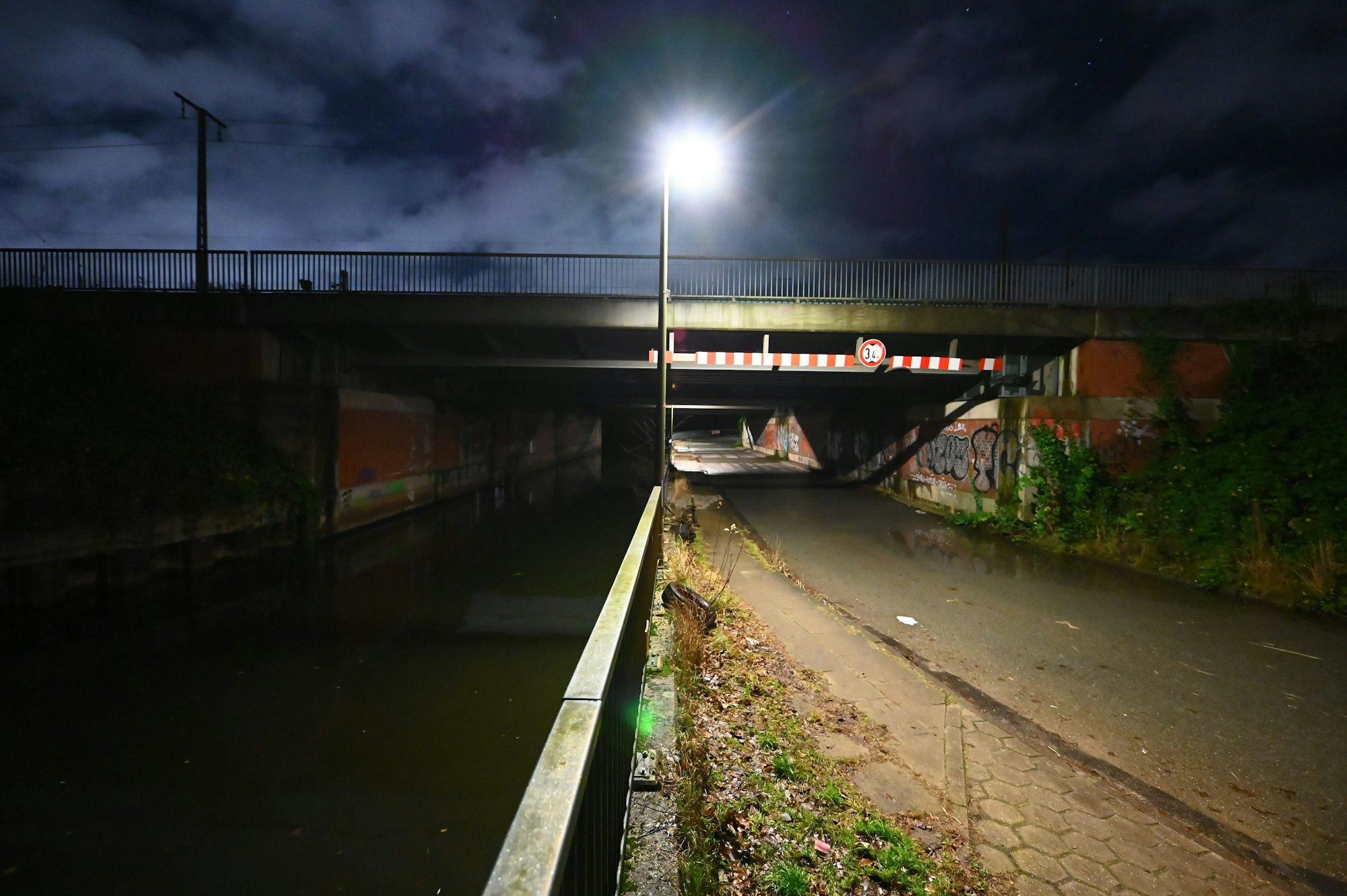 Der Ernst-August-Kanal unter Bahnbrücken an der Straße Vogelhüttendeich im dunkeln von einer Straßenlaterne angestrahlt.