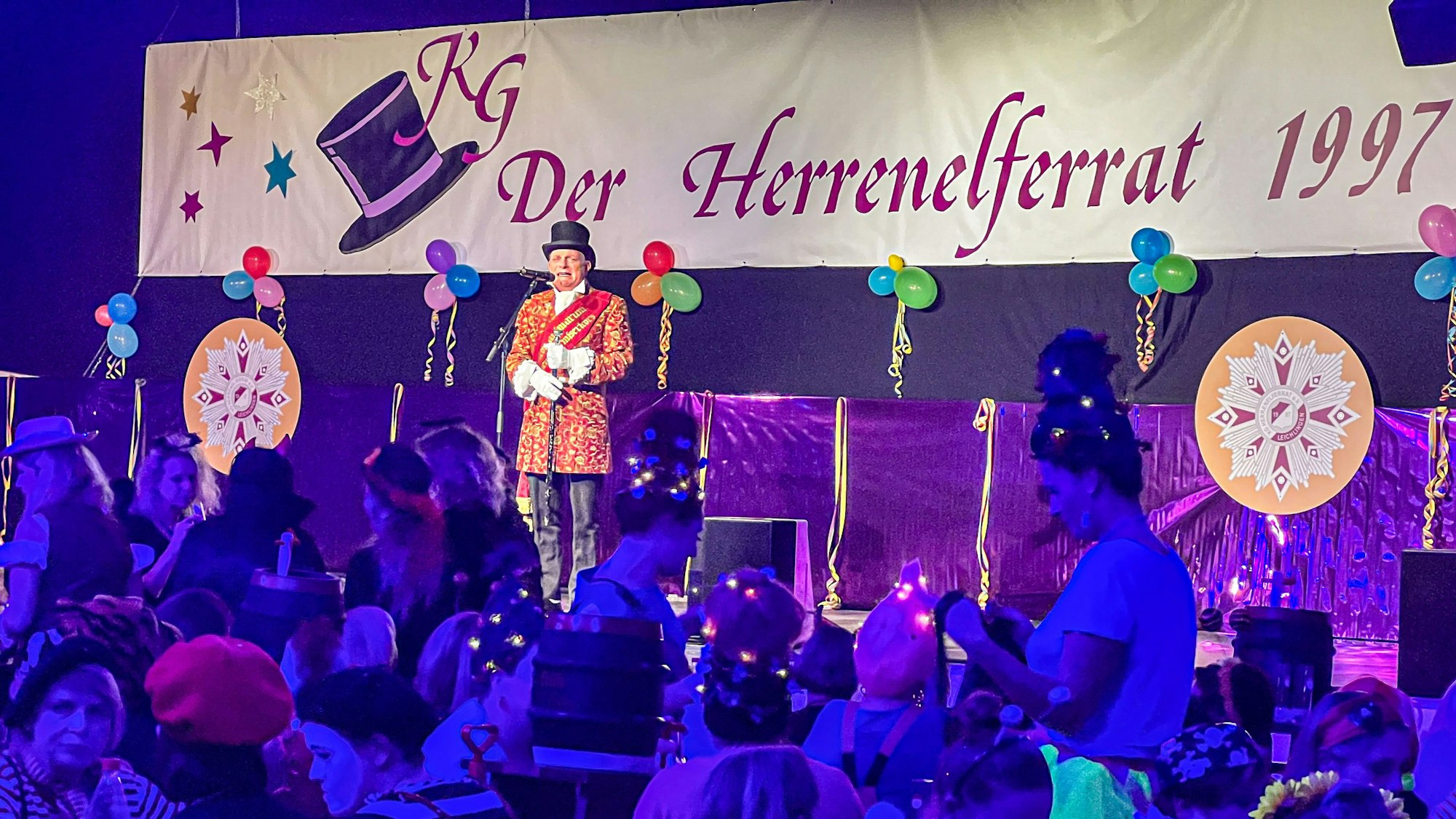 Der Büttenredner Dä Nubbel steht vor einem vollen Saal auf der Bühne und spricht in ein Mikrofon.