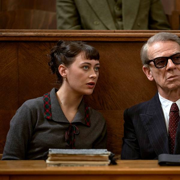 Toni (Mercedes Müller, l.) übersetzt für Gehlen (Martin Wuttke, r.) bei einer Verhandlung. Sie trägt ein graues Kostüm, er einen schwarzen Anzug und eine Sonnenbrille.
