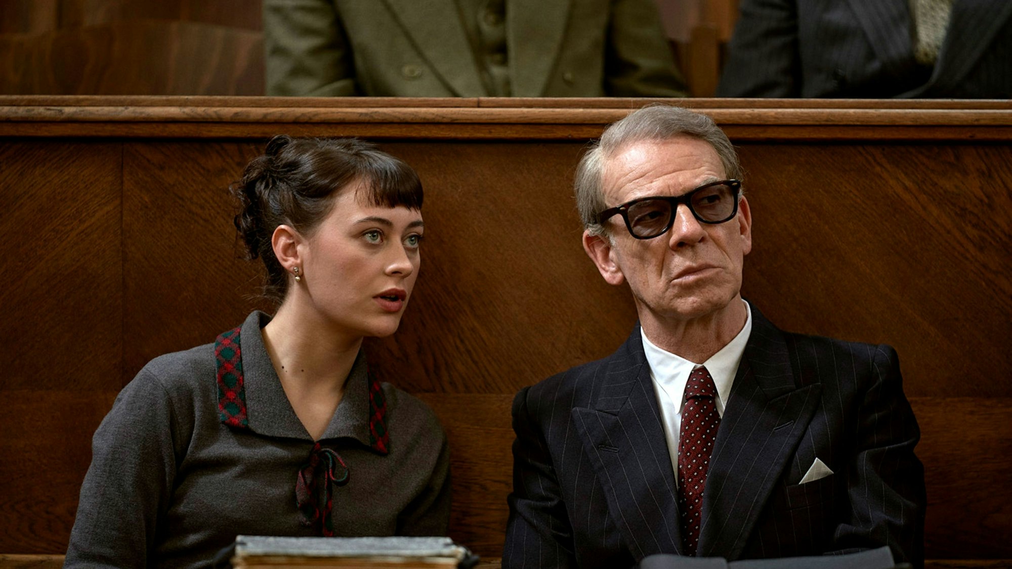 Toni (Mercedes Müller, l.) übersetzt für Gehlen (Martin Wuttke, r.) bei einer Verhandlung. Sie trägt ein graues Kostüm, er einen schwarzen Anzug und eine Sonnenbrille.