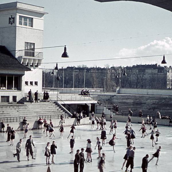 Menschen auf der Eisfläche. Links hinten im Bild ein Turm mit Hakenkreuz darauf.