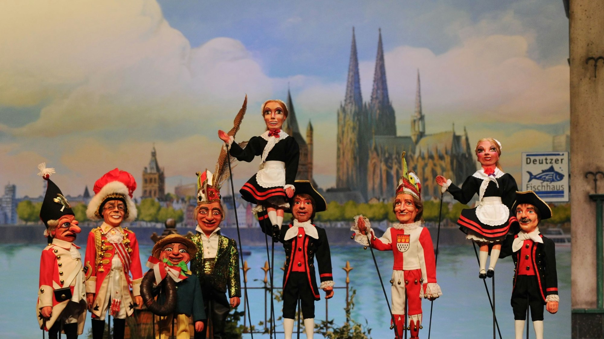 Stockpuppen des Hänneschentheaters vor dem Kölner Rheinpanorama: Rote Funken und Hellige Knäächte un Mägde posieren mit Speimanes und Sitzungsleiter Schäng.
