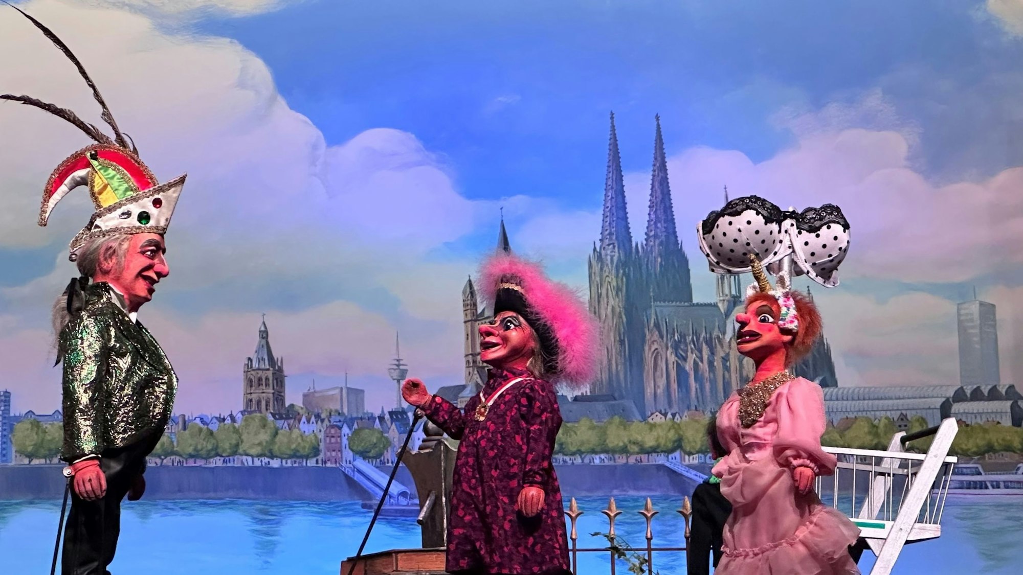 Zänkmanns Kätt und Köbeschen im rosa Kleid ziehen mit einem Riesen-BH am Einkaufswagen als „Feministische Volksfront Knollendorf“ durch Deutz, Sitzungspräsident Schäng (l.) versteht die Welt nicht mehr.