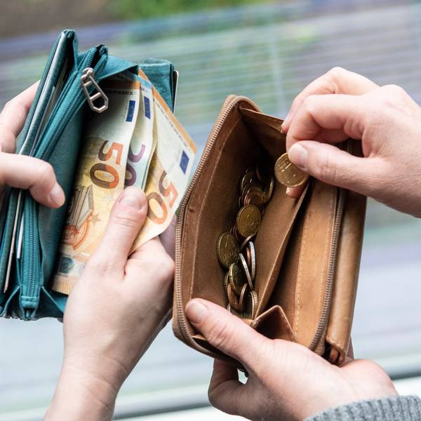 Zwei Menschen zeigen den Inhalt ihrer Geldbeutel. In einem sind Euro-Scheine (50er und 20er), im anderen nur Münzen.