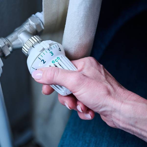 Eine Hand dreht am Thermostat einer Heizung