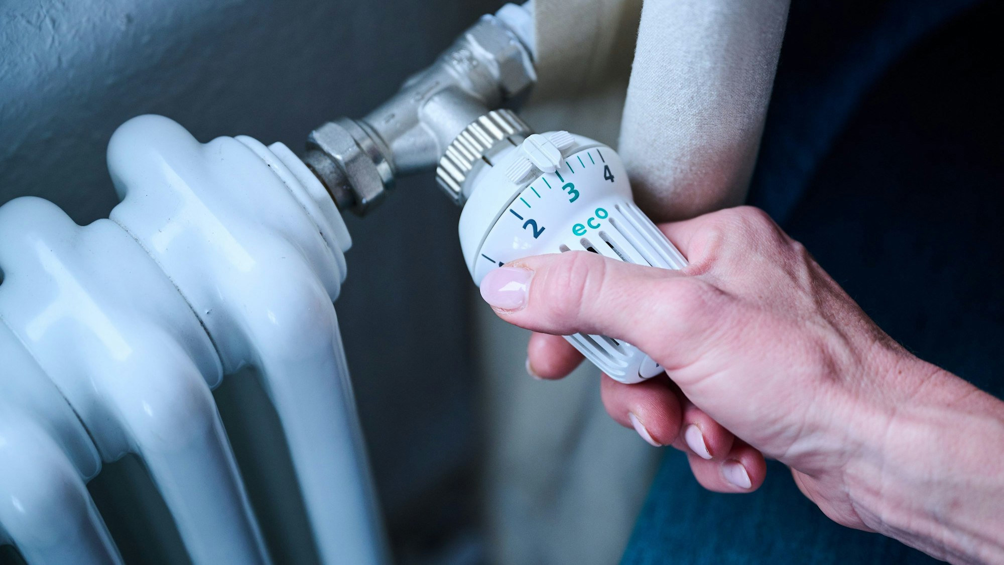 Eine Hand dreht am Thermostat einer Heizung