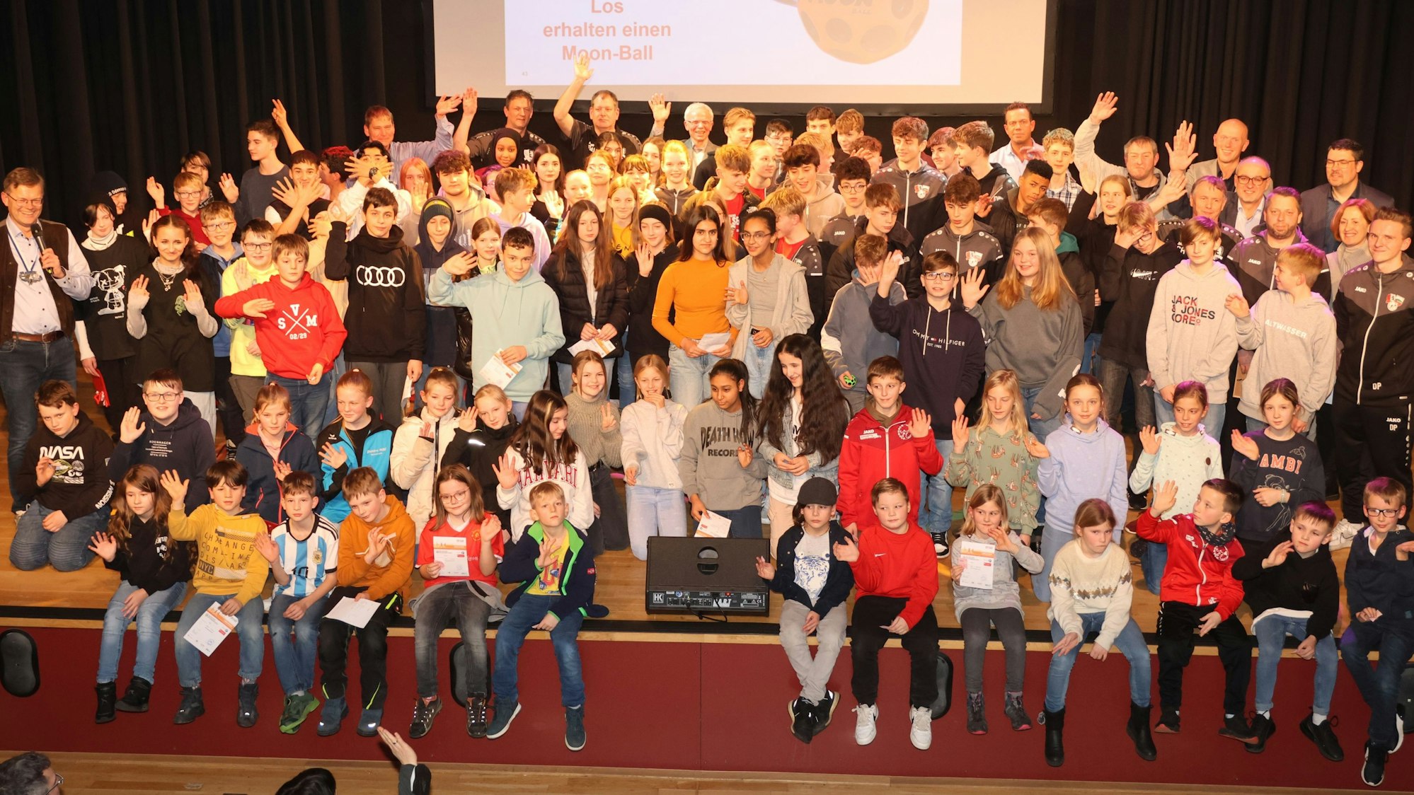 Auf einem Gruppenfoto stehen viele Erwachsene, Jugendliche und Kinder. Einige von ihnen reißen die Hände in die Höhe.