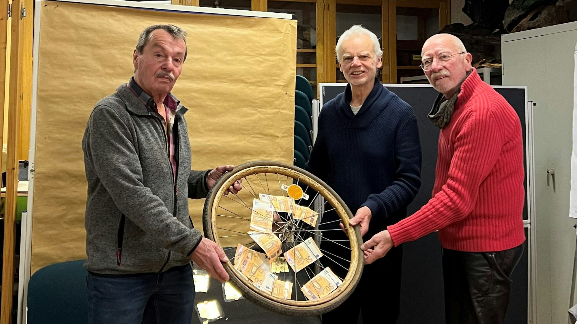 Die Ehrenamtlichen des Repair Cafés (r.) dem Verantwortlichen der Tafel (Jürgen Diers) das Geld für die Arbeit der Lebensmittelausgabe.