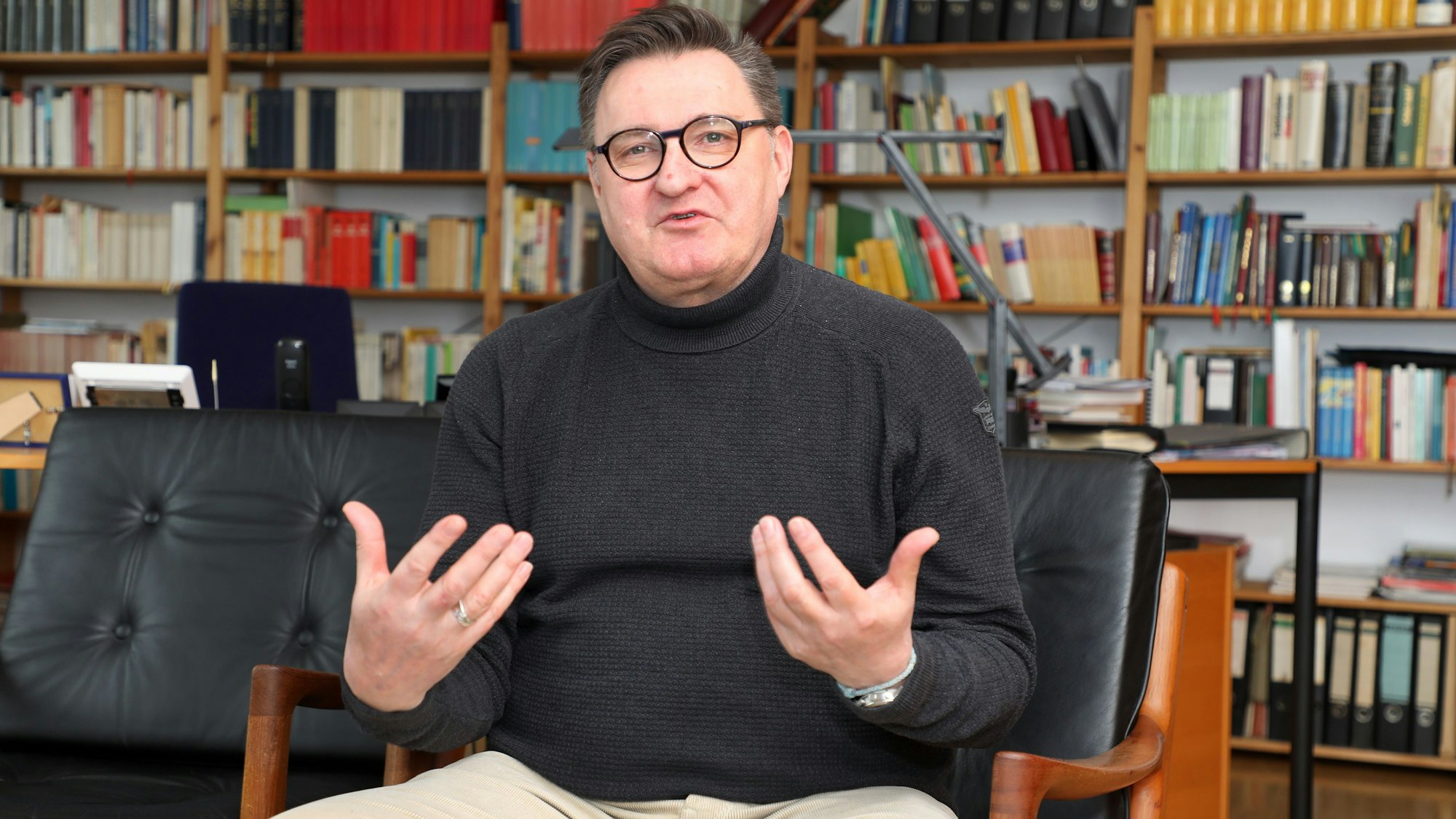 Norbert Hörter sitzt vor einer Bücherwand und gestikuliert.