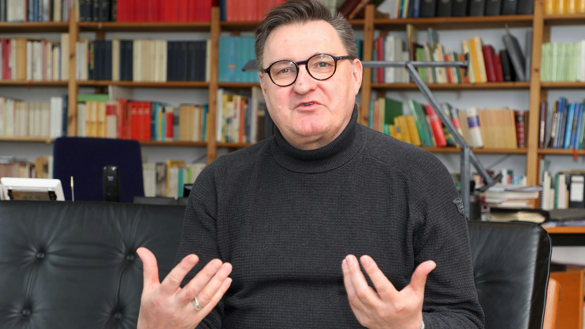 Der katholische Pfarrer und Kreisdechant Norbert Hörter sitzt in einem Sessel seines Arbeitszimmers vor einer Bücherwand und spricht.