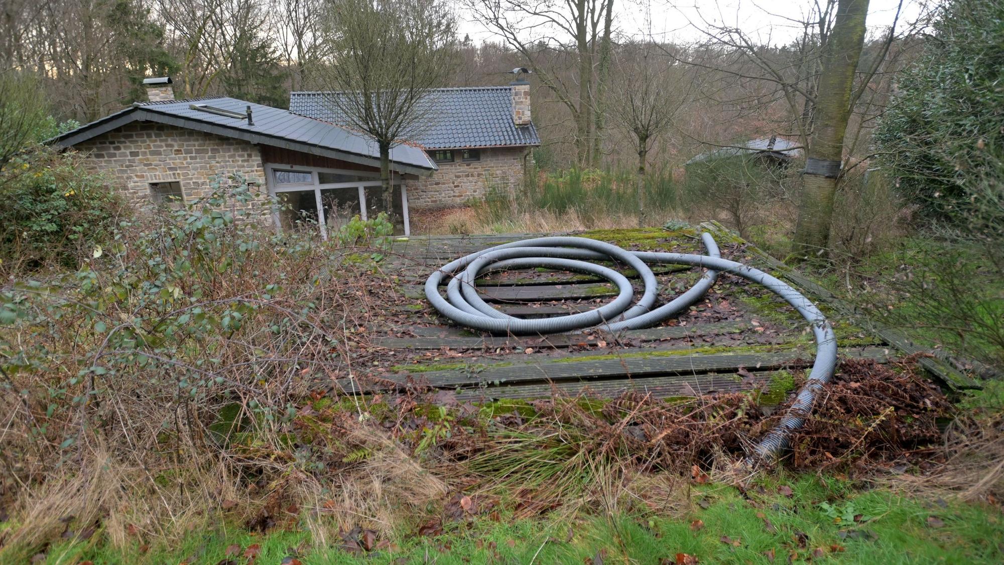 Ein Haus steht auf einem verwucherten Grundstück, eine Bretterbude erhebt sich im Vordergrund.