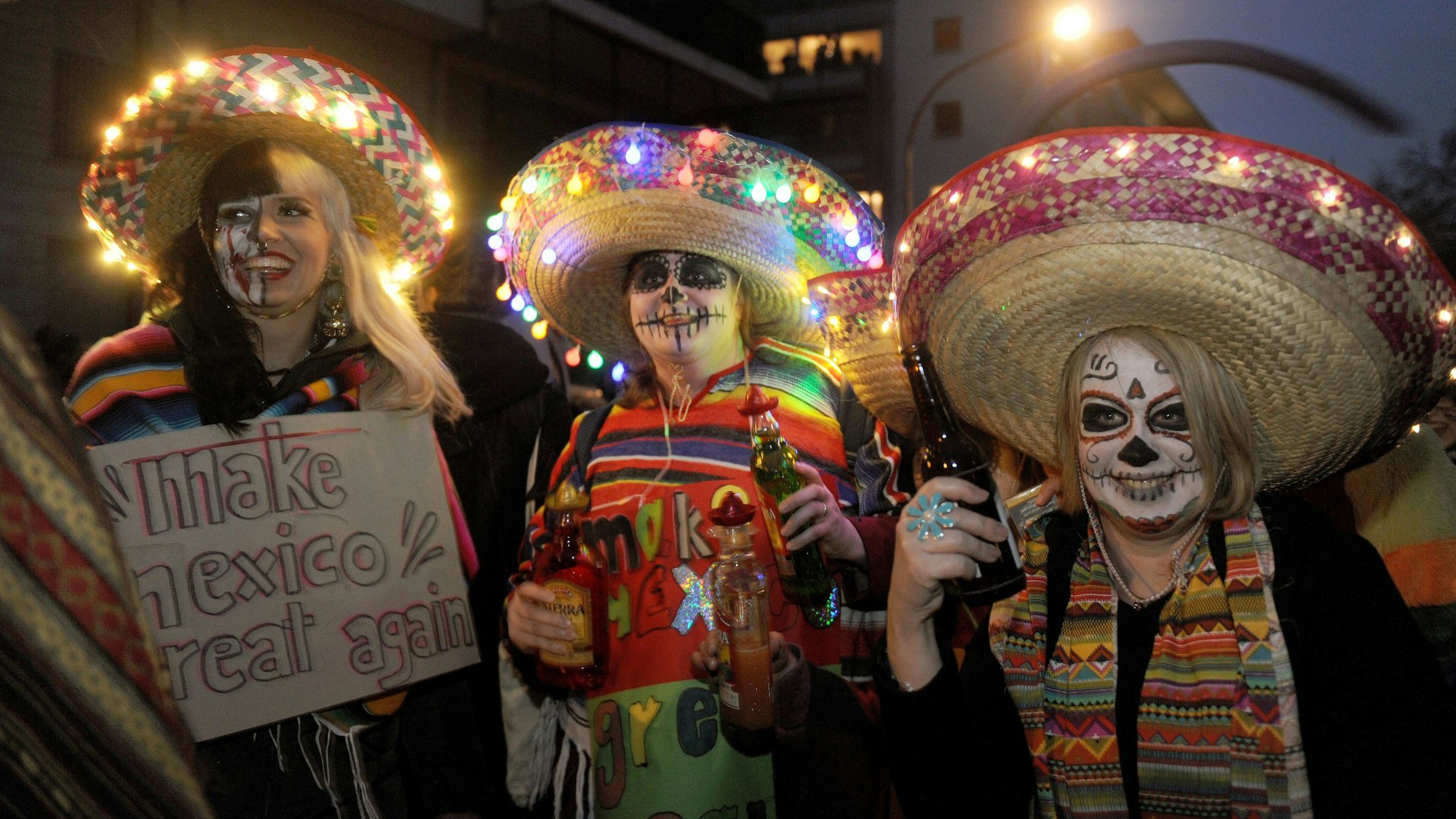 Drei als Geister geschminkte Menschen mit Sombreros mit Lichterketten.