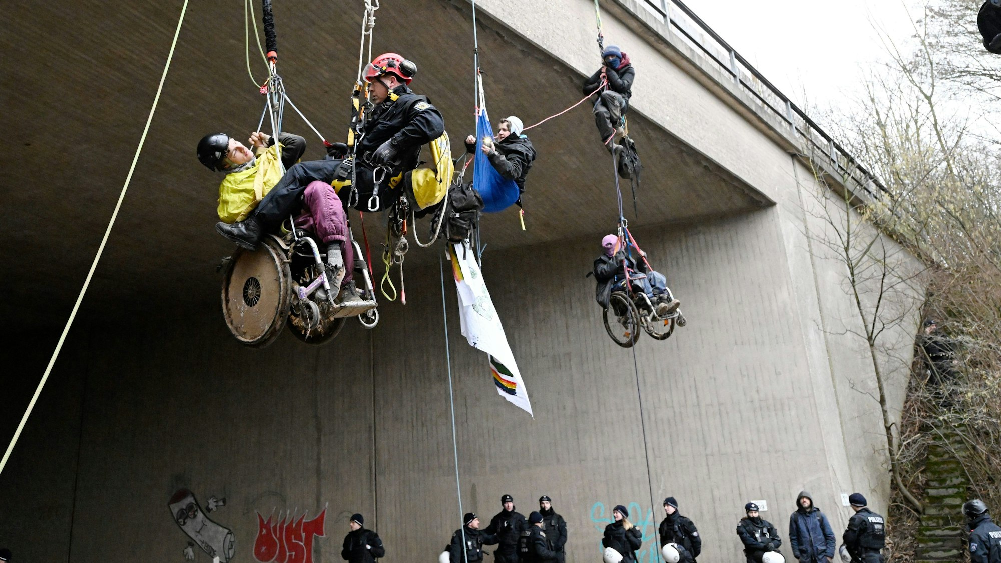 Ein Höhenretter der Polizei hilft einem Umweltaktivisten im Rollstuhl auf den Boden. Klimaaktivisten in Rollstühlen haben sich am Montagmorgen von einer Autobahnbrücke der A44 in der Nähe von Lützerath abgeseilt. Die Brücke liegt ungefähr vier Kilometer Luftlinie vom Braunkohleort Lützerath entfernt.