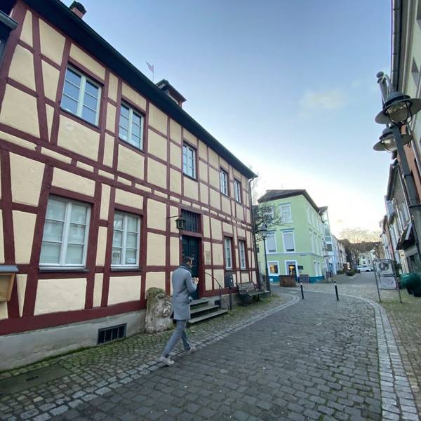 Ein Mann geht in einer Gasse über Kopfsteinpflaster an einem Fachwerkhaus vorbei.