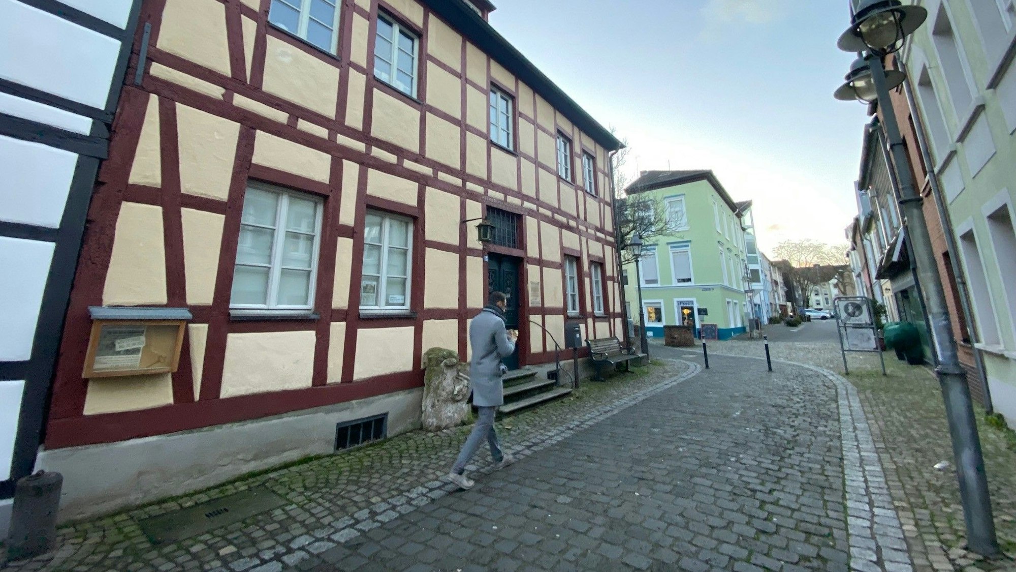 Ein Mann geht in einer Gasse über Kopfsteinpflaster an einem Fachwerkhaus vorbei.