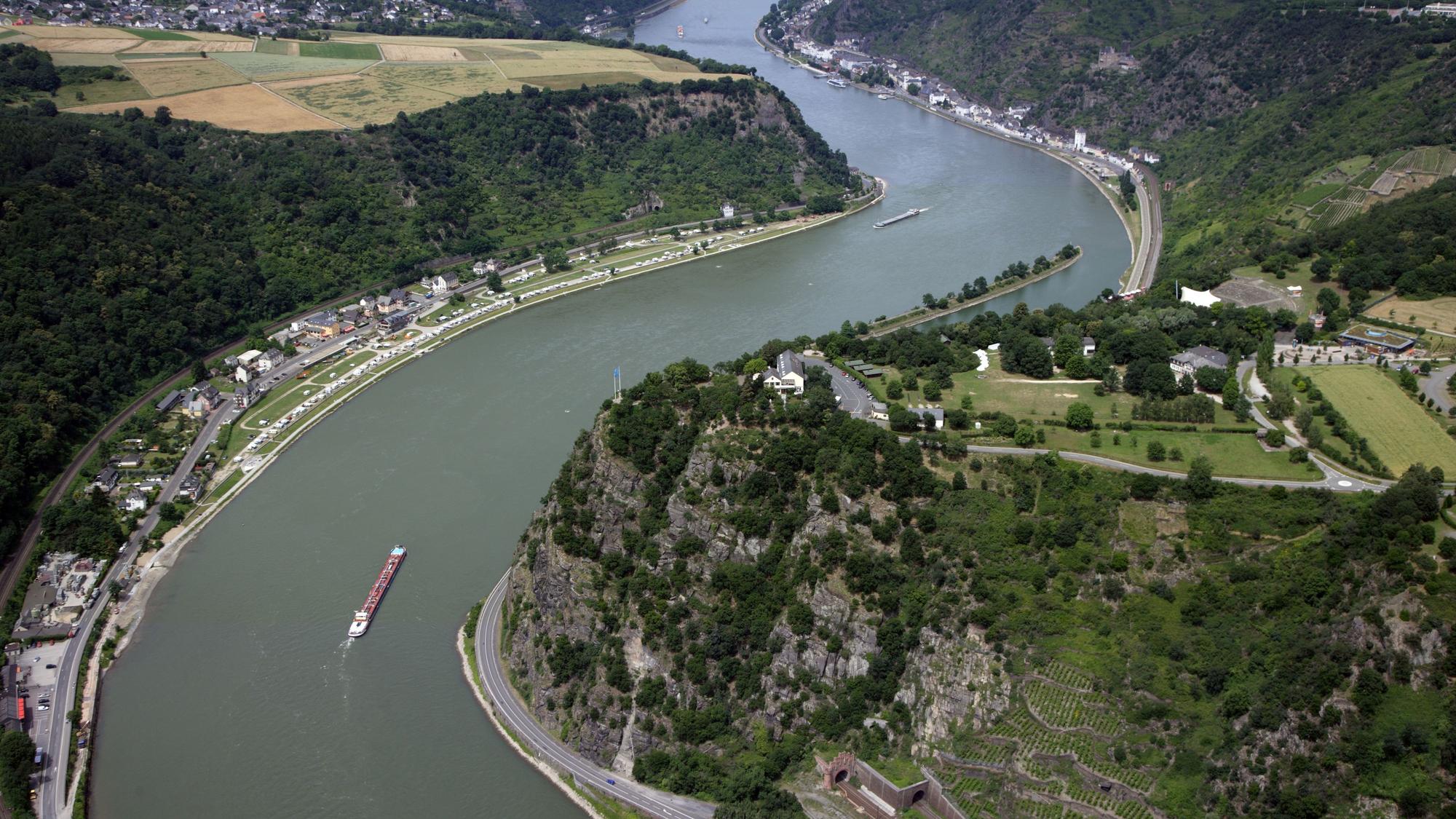 Der Rhein schlängelt sich durch die grüne Landschaft des Mittelrheintals beim Loreley-Felsen. Frachschiffte fahren auf dem Fluss.