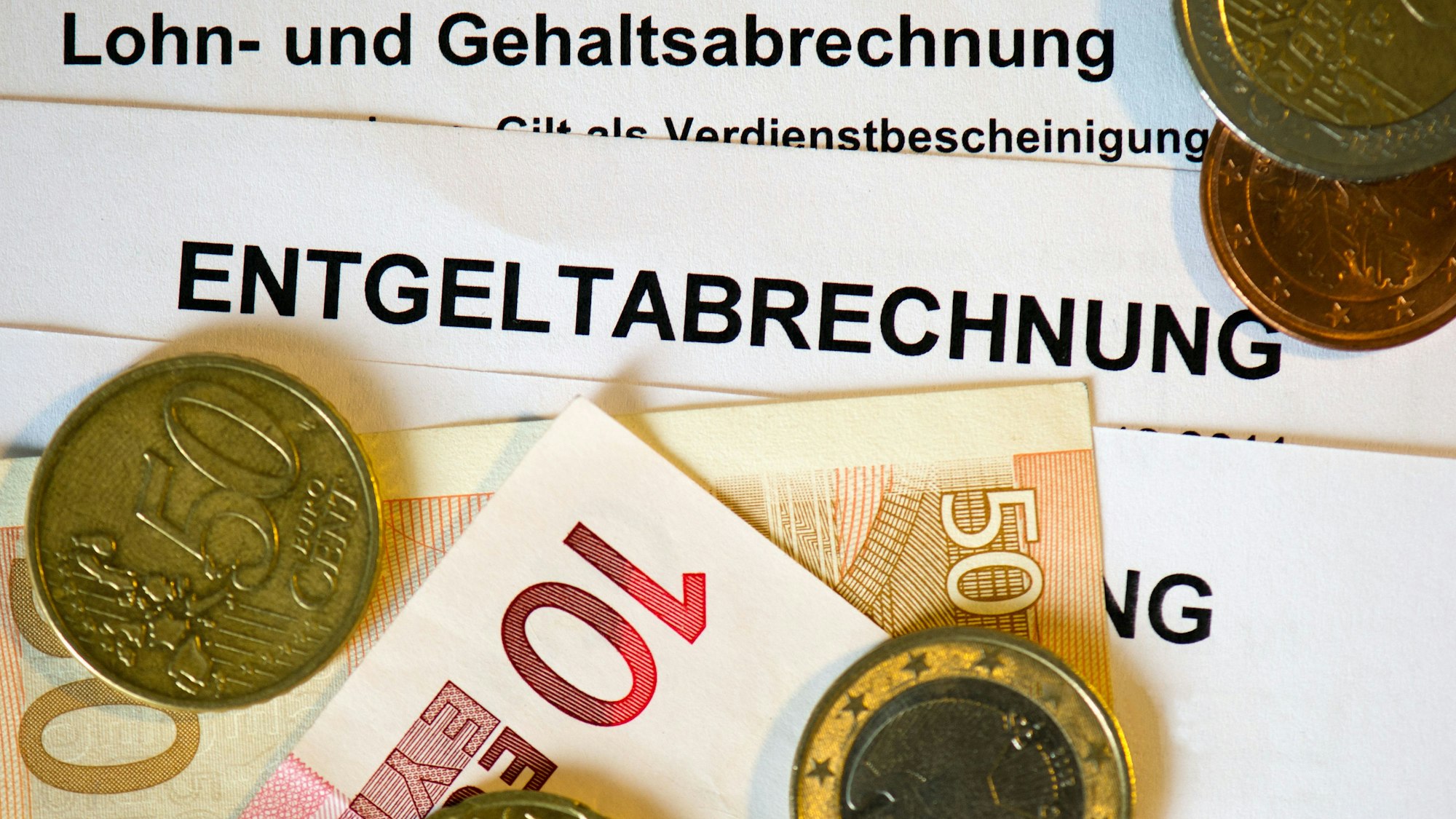Auf Lohn- und Gehaltsabrechnungen (Entgeltabrechnungen) liegen Euromünzen und Eurogeldscheine.