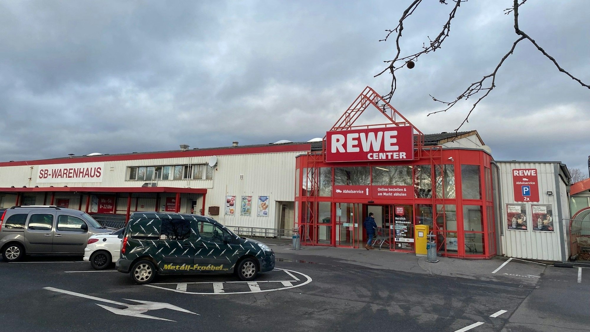 Vor dem Rewe-Center in Brühl-Ost parken Autos, ein Kunde schiebt seinen Einkaufswagen ins Geschäft.