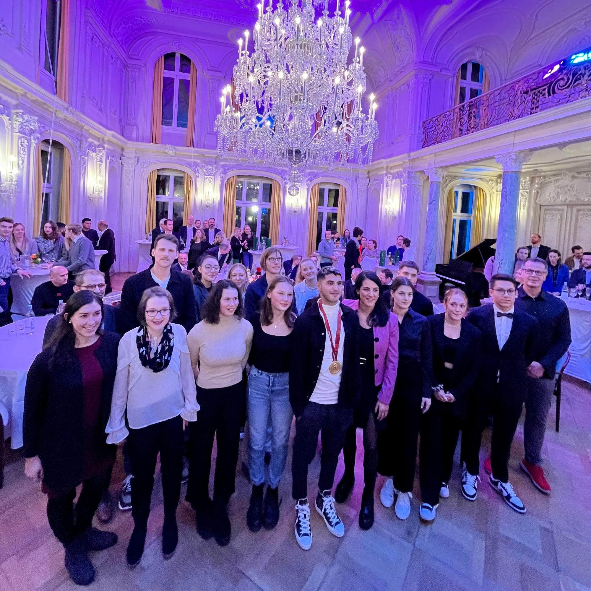 Eine Gruppe geehrter Sporter steht unter dem großen Kronleuchter im Spiegelsaal.