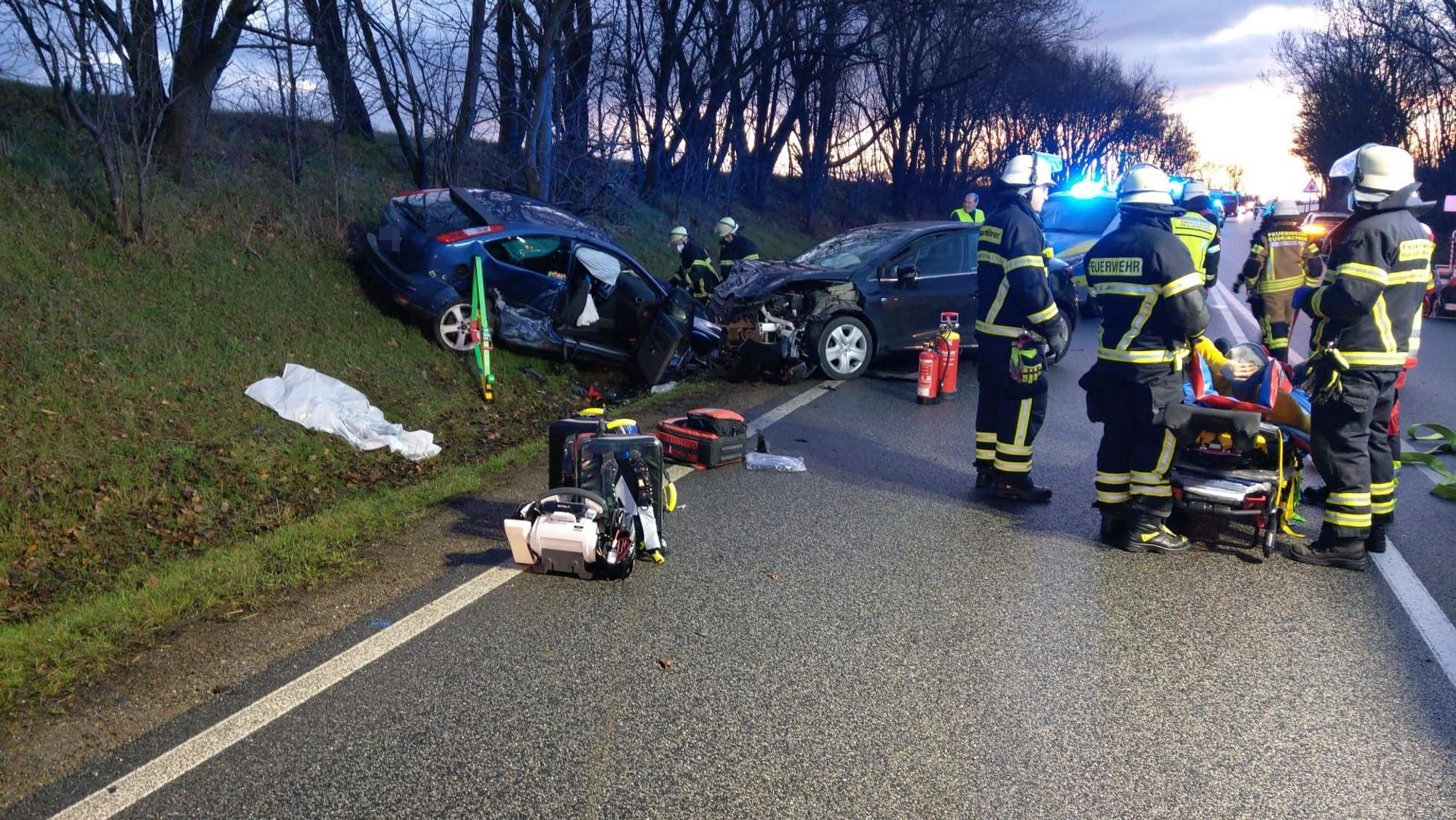 Mehrere Feuerwehrleute stehen an der Unfallstelle. Zwei Autos sind ineinander gefahren und stehen im Straßengraben.
