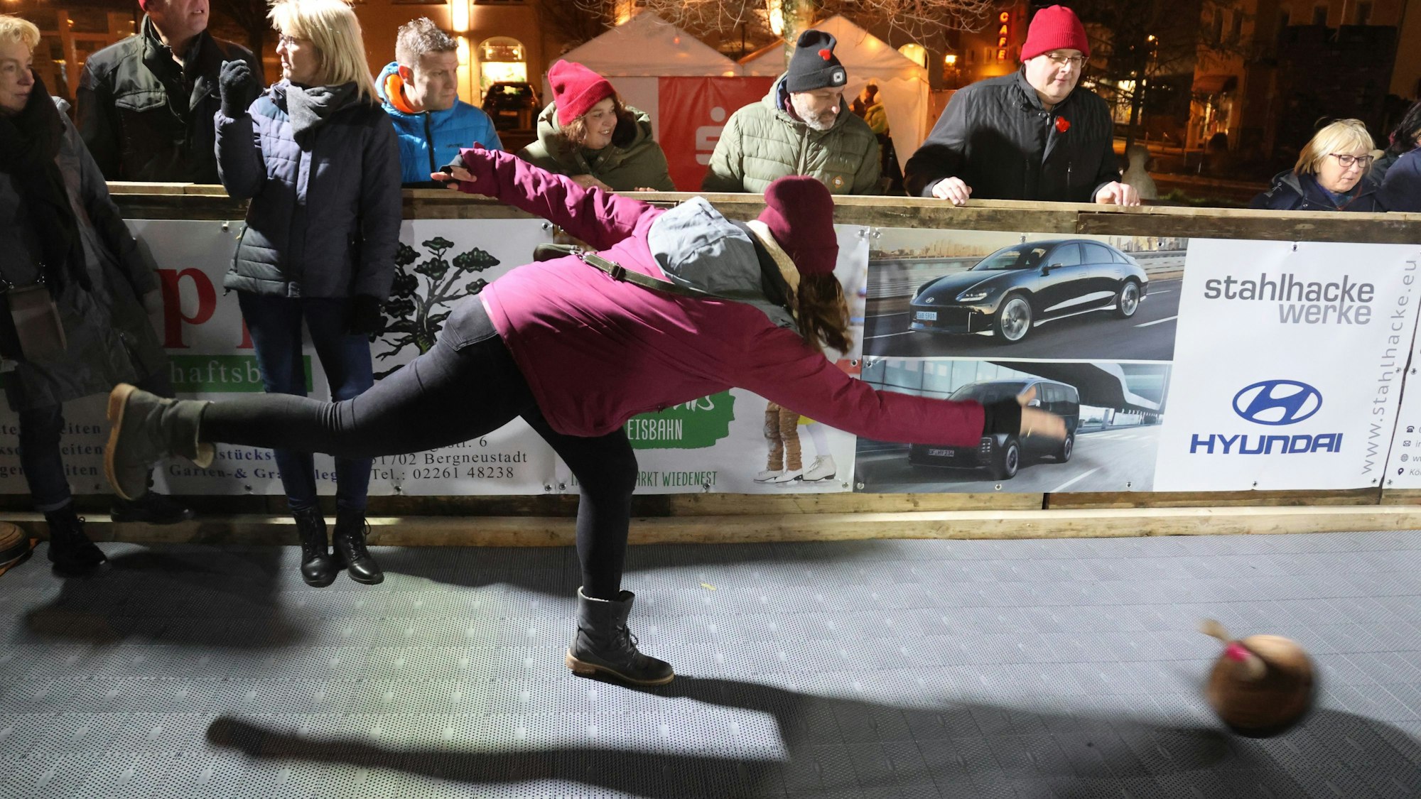 Zu sehen ist die Kunststoffbahn, die beim Bergneustädter Wintermärchen die Eisbahn ersetzt. Im Vordergrund wirft eine Frau mit dicker Jacke, Schal und Mütze einen Eisstock.