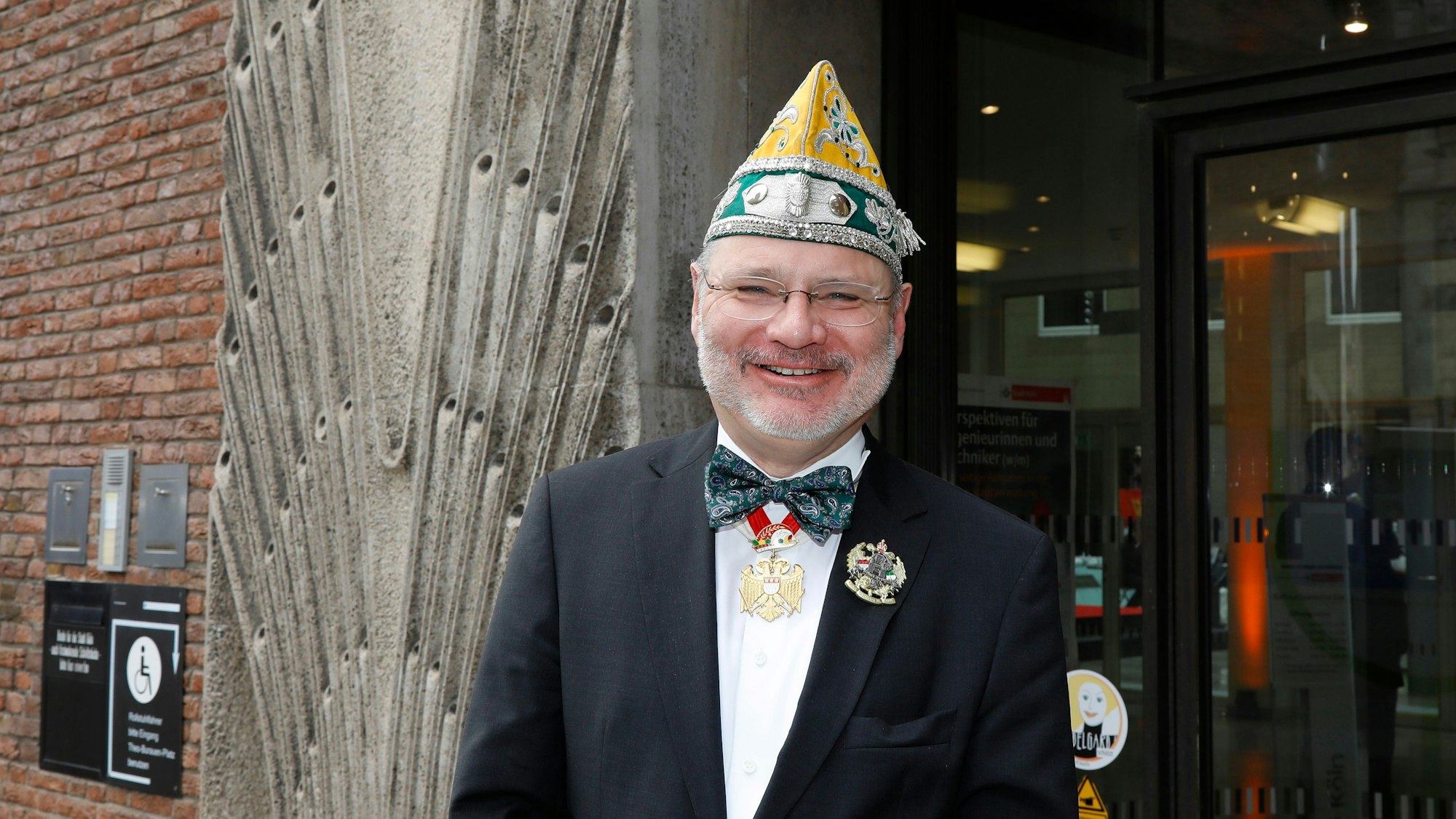 Willi Stoffel, Zugleiter schull- un veedelszöch, steht mit einer Mütze der Ehrengarde vor dem Rathaus.