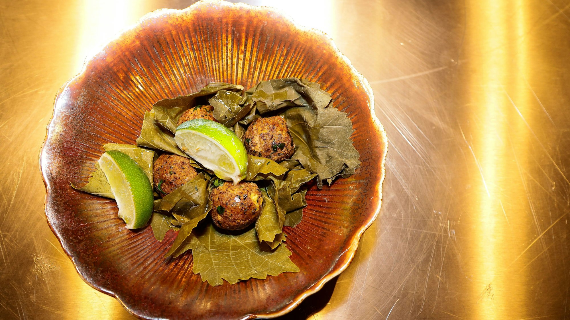 Auf einem Teller sind Bällchen aus Bulgur mit Weinblättern drapiert.