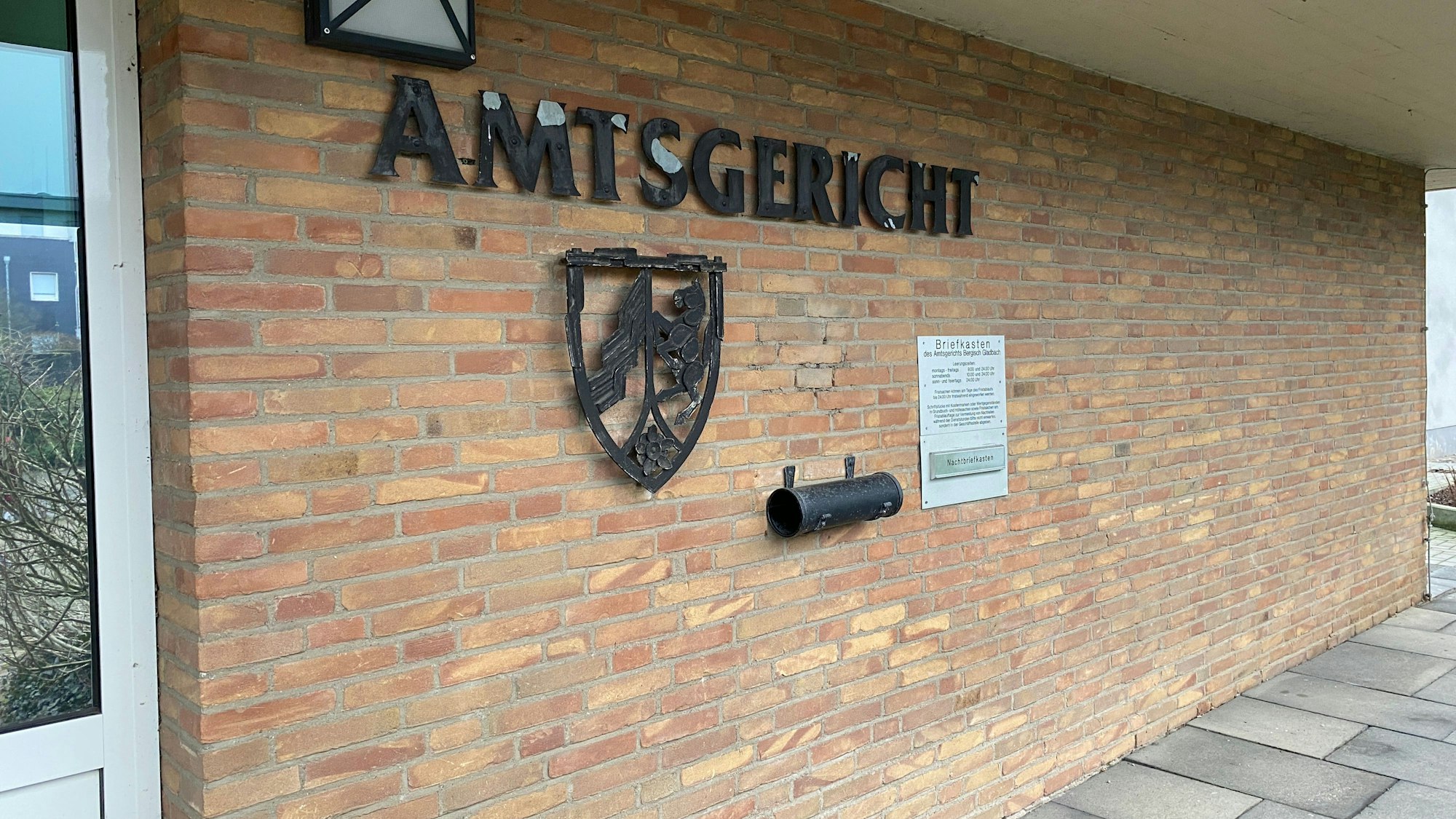 Die Front des Amtsgerichts in Bergisch Gladbach mit Backsteinmauer, Schriftzug und NRW-Landeswappen.