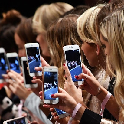 Frauen mit Smartphones filmen und fotografieren eine Modenschau.