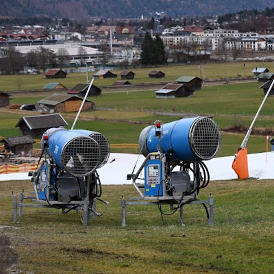 Schneekanonen stehen im Grünen neben einer Skipiste.