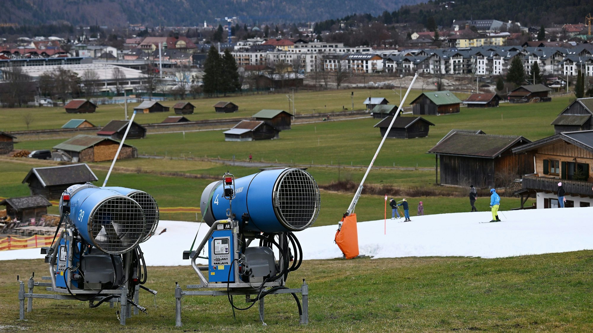 Schneekanonen stehen im Grünen neben einer Skipiste.